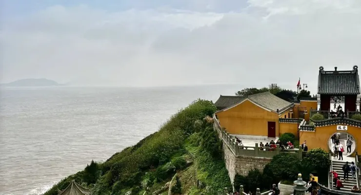 遠處可見海面。廟宇建築古樸,色彩鮮明,周圍綠意盎然。圖片的景致呈現出山與海的美麗結合,增添了詩意的氛圍。