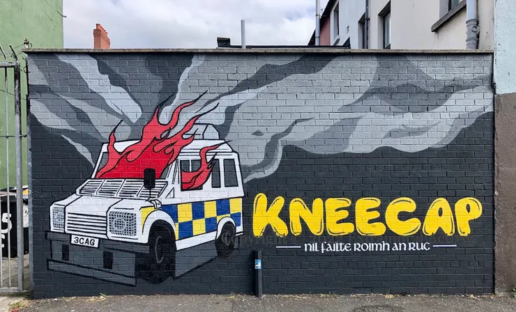 2022年8月，Kneecap在表演前發佈一張寫上「不歡迎RUC」，繪有著火警車的壁畫。此舉引來多個政黨抗議，表示壁畫煽動仇恨。圖源﹕Extramural Activity