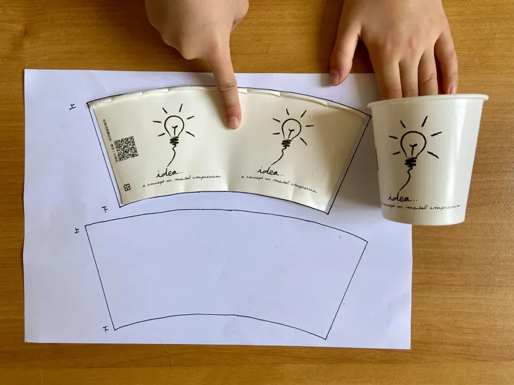 將紙杯沿著杯壁接縫處剪開，底部剪掉，在白紙上畫出杯壁形狀，杯緣線多延伸出去一點點，讓只稍長一些，貼上去較不容易有縫。