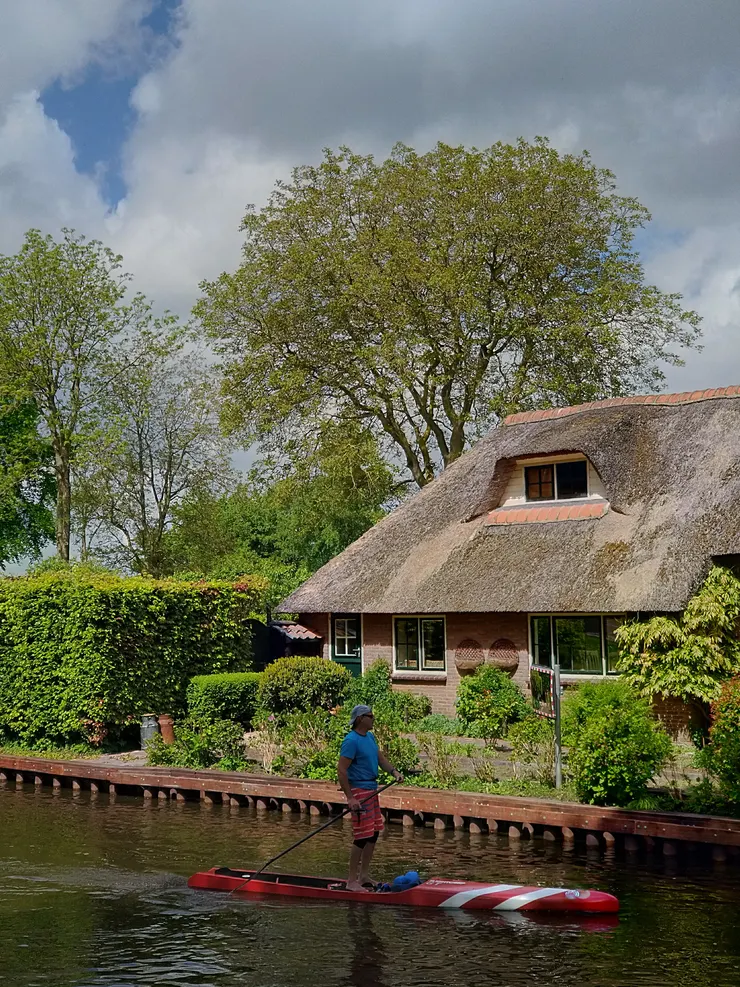 蘆葦草屋頂的老屋子前剛好一人划過