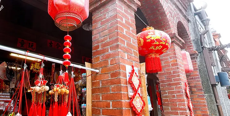 三峽老街店家前懸掛的紅色大燈籠，背景為販售紅繩掛飾與傳統童玩的雜貨店，充滿濃厚台灣復古情懷與過年過節氣息。