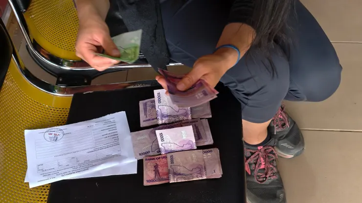 Christina認真的點算鈔票。由於鈔票面值小,當地習慣將9張鈔票疊成一疊後,用第10張鈔票夾起來。照片中紫色鈔票每疊是10萬先令。