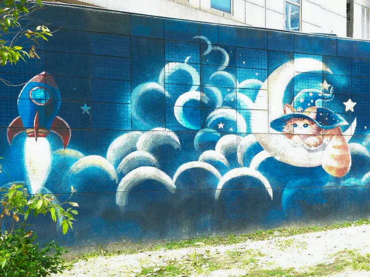 首先，這是充滿未來感的魔幻藍色星空牆，想不到這月亮上睡的不是嫦娥 ，而是一隻戴著巫師帽的貓咪 ！這貓咪似乎把月亮當嬰兒床。而在牠不遠處 ，一艘火箭正「轟」地一聲拔地而起