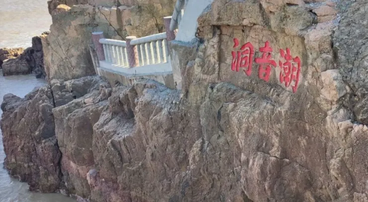 潮音洞入口處的岩石上刻著「潮音潮」的紅色字樣，旁邊有一條石階小徑通向洞口，背景是湛藍的海水和岩石。