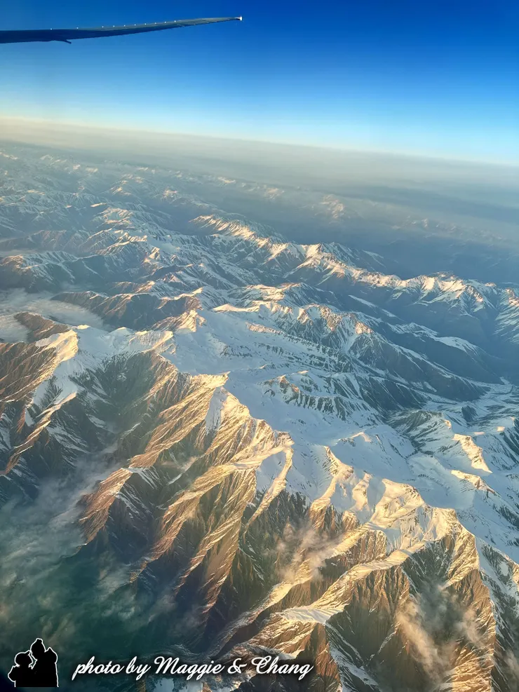 夕陽的金色光芒灑落在雪山上，讓整片山巒染上溫暖色調。白雪映著橘黃的霞光，層層山勢如畫卷展開，既壯闊又詩意，讓人不禁屏息欣賞。
