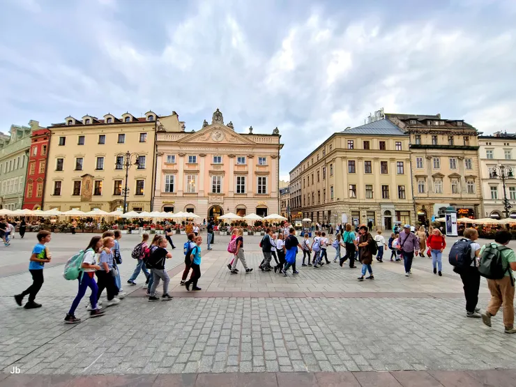 【集市廣場，遊人雖然不少，但在廣大空間下，絕無擁擠之感。背景可見歷史悠久的聯排別墅（Kamienice）與當年的貴族宅邸，現多為旅店或商家。 】