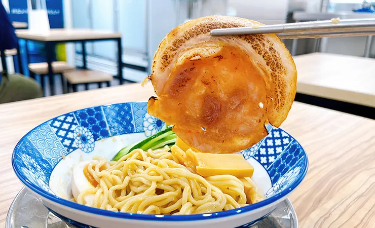 筷子夾起小白拉麵乾拌麵專屬的厚切叉燒，肉質軟嫩帶有油花與焦香，內湖必吃拉麵配料。