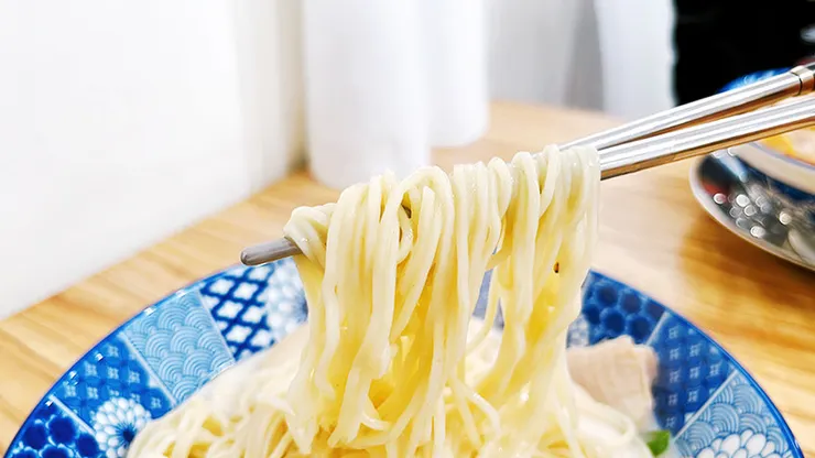 筷子夾起沾滿雞豚白湯的日本細麵條，展現小白拉麵麵條的Q彈與極佳的吸湯力。