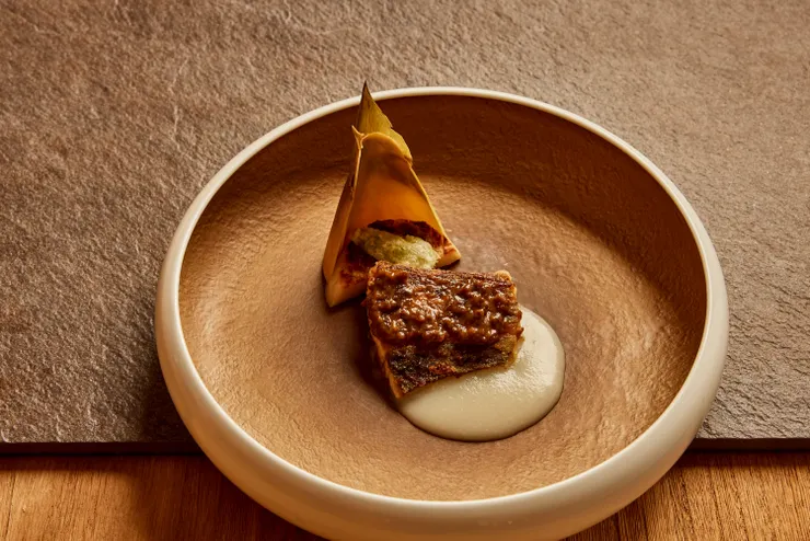 「款冬味噌燒鰆魚 新洋蔥醬」將鰆魚以油封低溫慢熟手法，熟度精準保留在半生熟質地，佐以日本款冬味噌與春季新洋蔥醬汁。