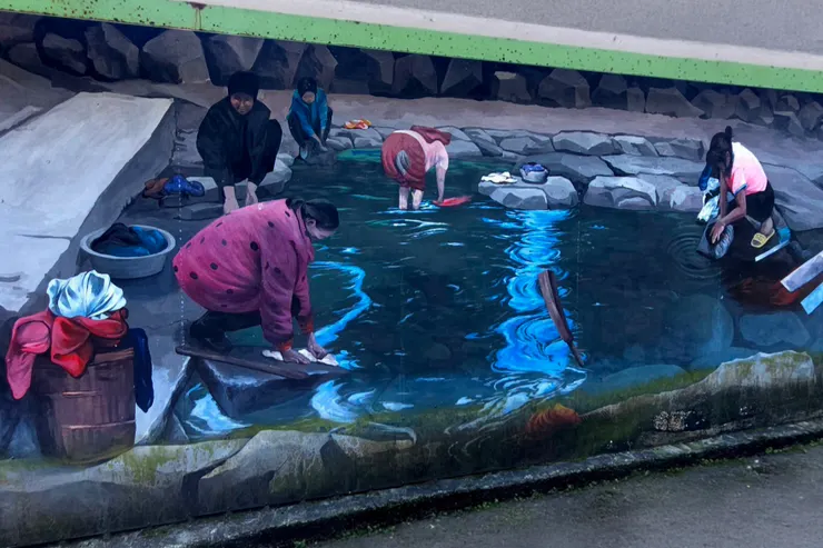 清溪浣衣，歲月悠長 晨曦微露，山佳的溪畔已響起了規律的擣衣聲。婦人們蹲踞在青石板上，雙手在清澈見底的溪水中起伏，揉搓出生活的韌性。水面上，紅衣與藍衫交織成最樸實的風景。