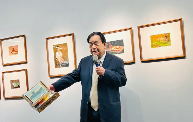冉老師拿著自己外出作畫使用的油畫箱，講解畫作