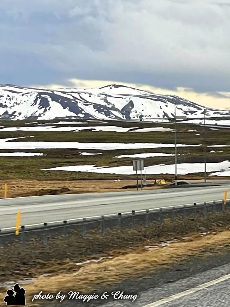 車窗外的風景從灰白城市漸漸轉為荒涼與壯闊。冰島的山景如畫，車子沿著南岸公路奔馳，路邊是覆雪的火山、黑色的熔岩地、偶爾冒出蒸氣的地熱田，這個國度有種不合時宜的寂靜與宏大，讓人看著看著，心也靜了。