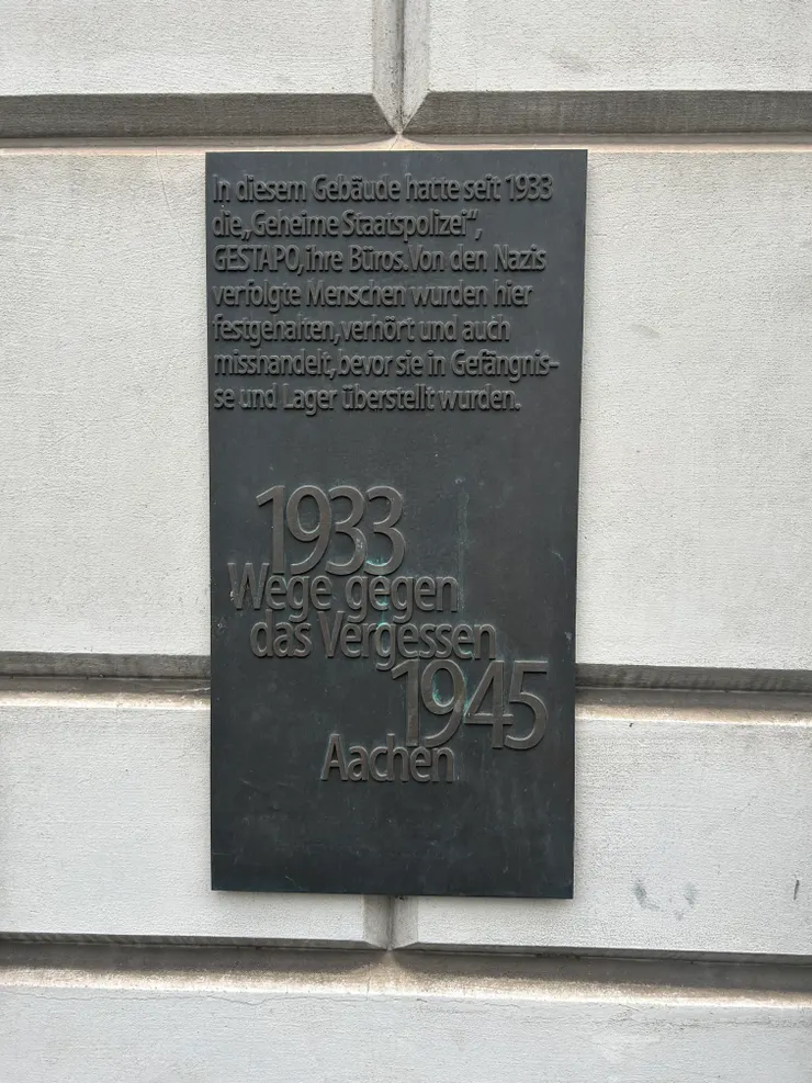 「1933 年起，這棟建築物被作為秘密警察的辦公室，被迫害的人們入獄或轉送集中營之前，曾在這裡遭到納粹逮捕、審問與虐待。」 阿亨大劇院旁的轉型正義告示。