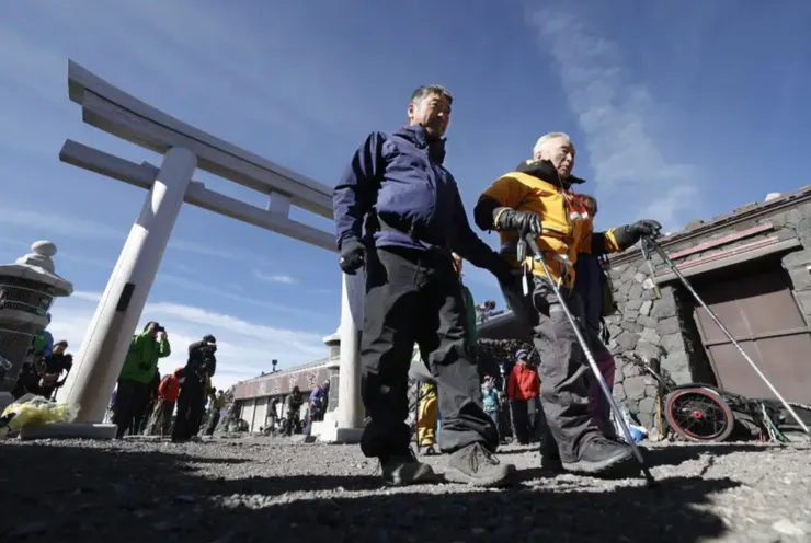 三浦雄一郎在親友攙扶下穿過富士山的鳥居，圖片擷取自日本共同社。