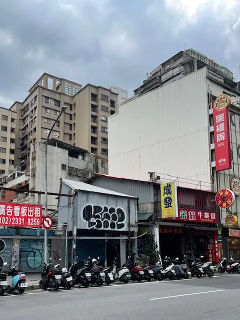 台北，住宿飯店對面的一排機車和半新舊建築物。