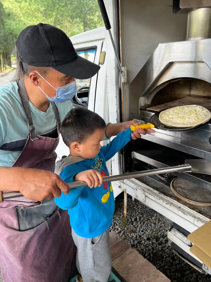 老闆帶小朋友手送餅皮進烤箱(第一次預烤起司)