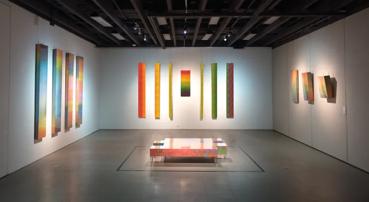 積吶虹光〈西方教堂-彩虹之約(博愛) 〉: 空間以鮮豔的色彩和垂直懸掛的畫作組成，宛如一座「彩虹教堂」，給人一種神聖和心靈慰藉的感覺。畫作以豐富的色調展現，從鮮紅、暖橙到翠綠和深藍，這些色彩層層疊疊，如同教堂彩窗上的光線投射，散發著溫暖與寧靜，象徵博愛精神。