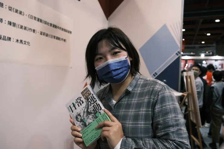 拿著作品《日常運動》的梁莉姿。黑色短髮、格子襯衫的造型及柔和堅定的眼神，更接近她受訪時的形象，只差了一副黑框眼鏡。圖片來源：梁莉姿提供