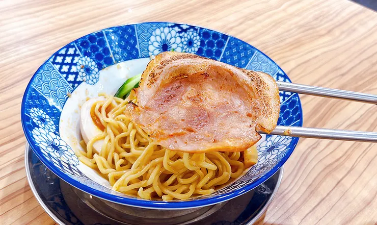 筷子夾起小白拉麵乾拌麵專屬的厚切叉燒，肉質軟嫩帶有油花與焦香，內湖必吃拉麵配料。