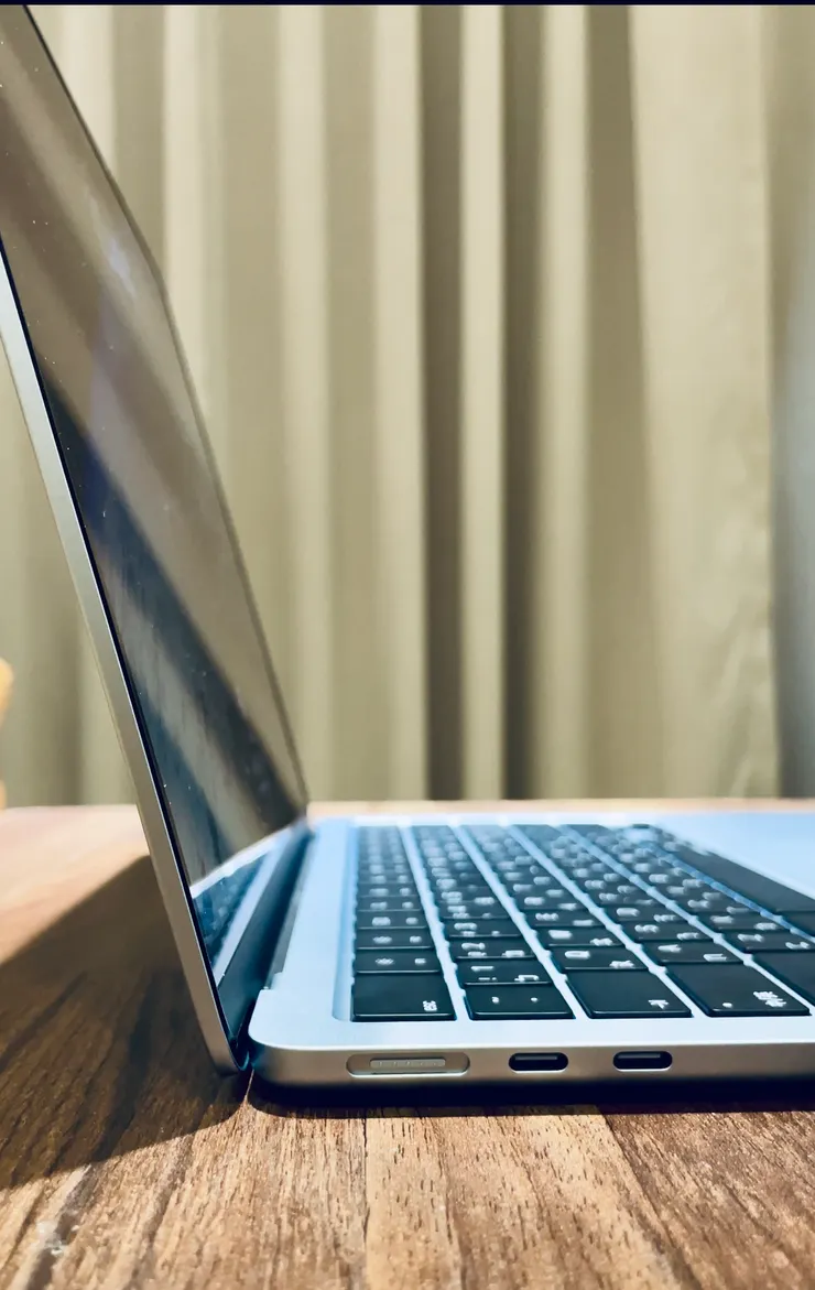 MacBook Air M4 機身側邊配備 MagSafe 充電孔與兩個 Thunderbolt 連接埠，輕薄機身下仍保留完整擴充性。金屬邊角與天藍色外殼在燈光下呈現柔和光澤，是科技與美學兼具的設計。