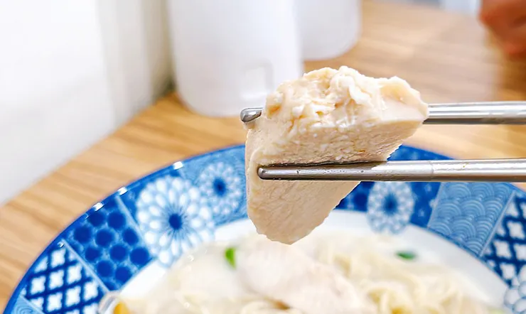 筷子夾起小白拉麵的厚切舒肥雞胸肉，肉質潔白細緻，展現軟嫩多汁的誘人質地。