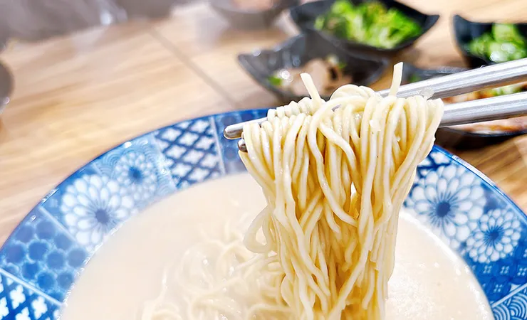 筷子大口夾起小白拉麵的15秒日式細麵，完美吸附蒜味豚骨湯汁，展現職人級Q彈與俐落口感。