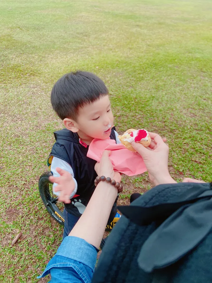 孩子在草皮上玩耍，品嚐著初春湧現的粉紅泡泡的甜點，這畫面是一種甜蜜的感受。