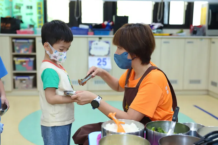 （圖說：中午裝飯食，教保員向皓皓介紹放在盤中的料理，讓他認識新的食物，降低挑食的情況。）