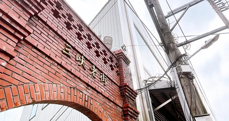 三峽老街標誌性的紅磚拱門近照，金色字體「三峽老街」鑲嵌於紅磚牆面，展現台灣傳統建築的古樸美感與歷史氛圍。