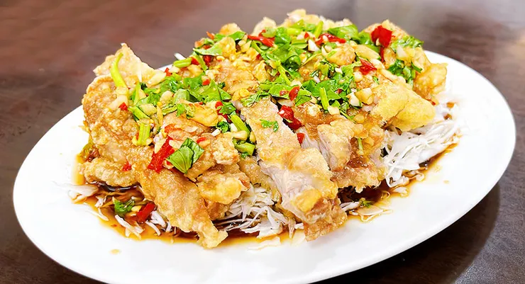 椒麻雞近拍，展現沾滿泰式酸辣醬的炸雞外皮，點綴新鮮香菜與辣椒。