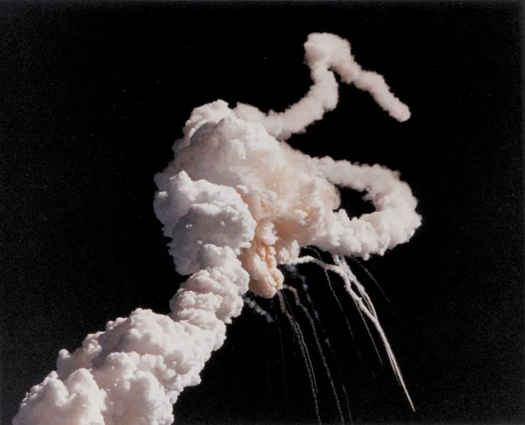 Challenger's solid rocket boosters fly uncontrollably after the breakup of the external tank separated them from the shuttle stack. The remains of the orbiter and tank leave thin white trails as they fall toward the Atlantic Ocean.