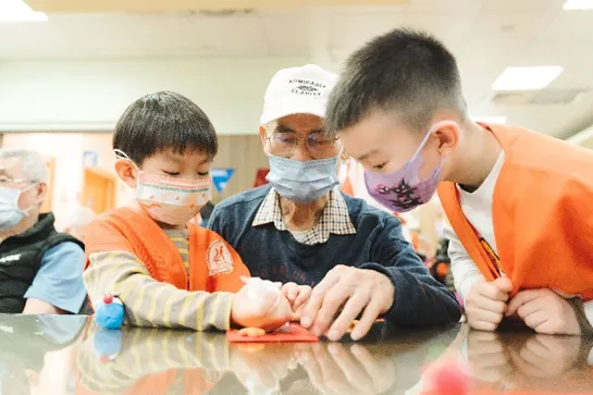 小志工教長輩擺放作品，老幼共融成為最美的風景。