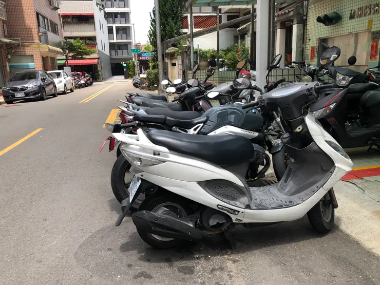 路邊沒有線的區域，大家都整齊的停車，然後左邊遠方有一台違停汽車（紅線）。你可發現這堆白牌裡面，其實藏了一台BMW 1200cc水平對臥紅牌？請問超出的部分（牌架），是不是不顯眼到不特別講看不太出來呢？這才是除台灣以外的全世界國家，停放機車最自然的日常，希望台灣也能盡快跟上。