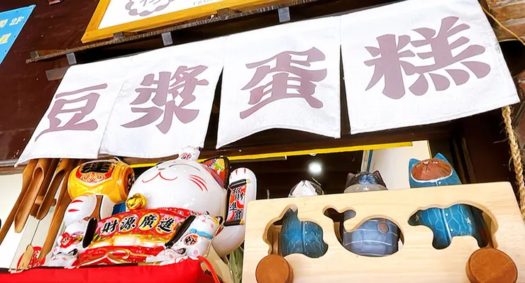 三峽初蛋糕店門口近景，上方掛有「豆漿蛋糕」白色掛布，前方裝飾巨大招財貓與木製貓咪造型擺飾，充滿文青與日式雜貨風情。