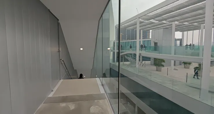 斜角玻璃廊道與淺灰牆面，綠美圖以簡約線條營造沉靜的行走體驗