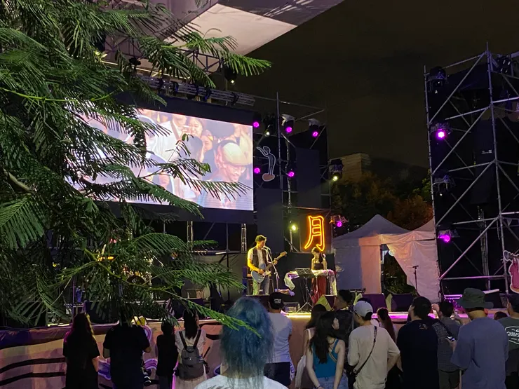 左側為樹影，舞台中間為背著吉他的鳳小岳。