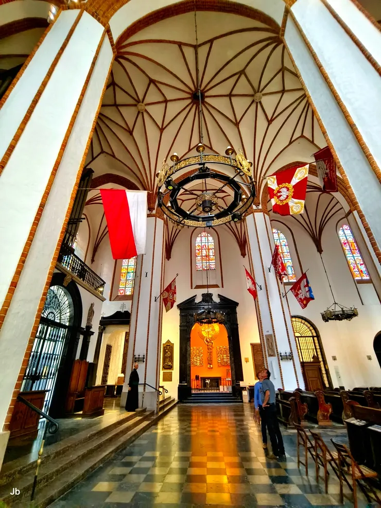 【聖若望主教座堂內部！深色大理石門框後方的亮橘色祭壇，供奉著著名的巴雷奇科十字架（Baryczko Cross）。這座哥德式耶穌受難像於 1525 年由商人 Jerzy Baryczko 從紐倫堡帶到華沙，被當地人視為神聖且具有奇蹟力量的象徵。】