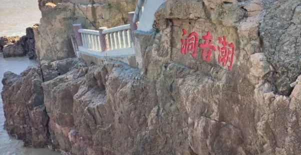 潮音洞入口處的岩石上刻著「潮音潮」的紅色字樣,旁邊有一條石階小徑通向洞口,背景是湛藍的海水和岩石。