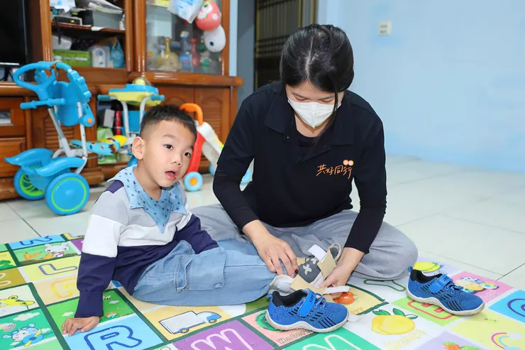 （圖說：練習用助行器步行前，教保員徐鈺喬為睿睿穿上踝足部支架，減少站立時因張力引發的不穩定性，以及跨步時的垂足情況。）