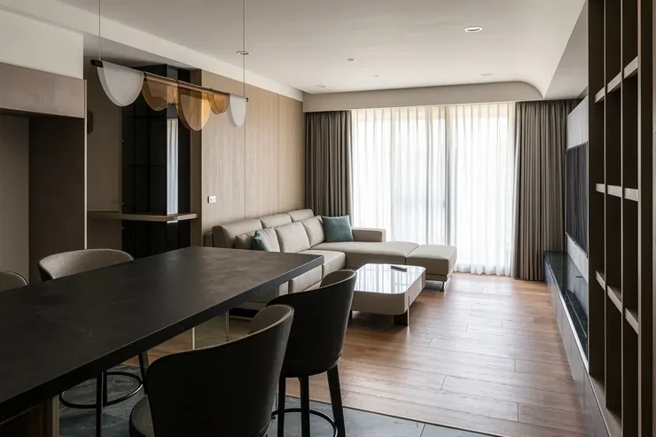 玄關走廊望向客廳，左側斜牆切角展示櫃，遠端銀狐石材電視牆