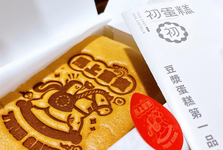 初蛋糕文青風格金黃禮盒與原味豆漿蛋糕全景，展現蛋糕剛出爐的蓬鬆感與精緻包裝，適合做為送禮推薦。