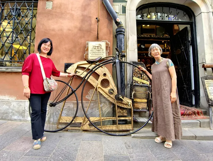 【表姊妹在舊城區著名古董店 Lapidarium (Lapidarium Jacek Kiliński) 門口。 該店創立於 1974 年，是極受歡迎的打卡地點。標誌性的復古高輪自行車（Velocipede）和木製紡車是該店的招牌裝飾。 】