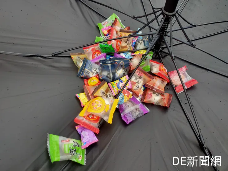 民眾用傘具接住罾子船上丢擲的麻糬和糖果。(記者曾金萬/攝)