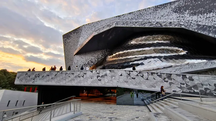 【晚霞山丘飛鳥巨蟒在洞穴中隱身！愛樂廳外牆及內、外地板都舖著山丘、飛鳥形狀的磁磚，而遠遠望去，建築主體似有隻巨蠎盤身在幽暗的洞穴中，鱗片閃閃發光。】