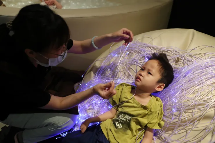 （圖說：在多感官教室中，教保員鄒伶儷(左)透過流瀑光纖提升樂樂的視覺反應。）