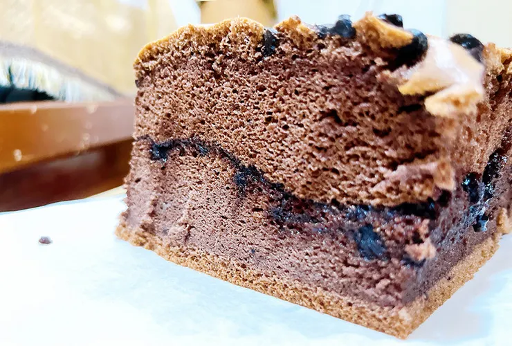 手拿一塊初蛋糕巧克力口味的側拍，指尖輕壓展現蛋糕的蓬鬆彈性，與中間流動感的巧克力醬細節