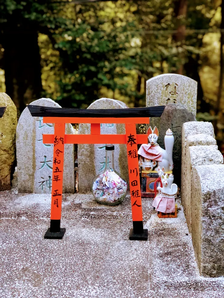 在山道深處，一座迷你的鳥居前，狐狸神靜靜守護，旁邊是一瓶折紙鶴，彷彿封存著無數心願。應該那是位信徒親手摺下的祈禱，將願望化為羽翼，寄存在神域與人間之間。