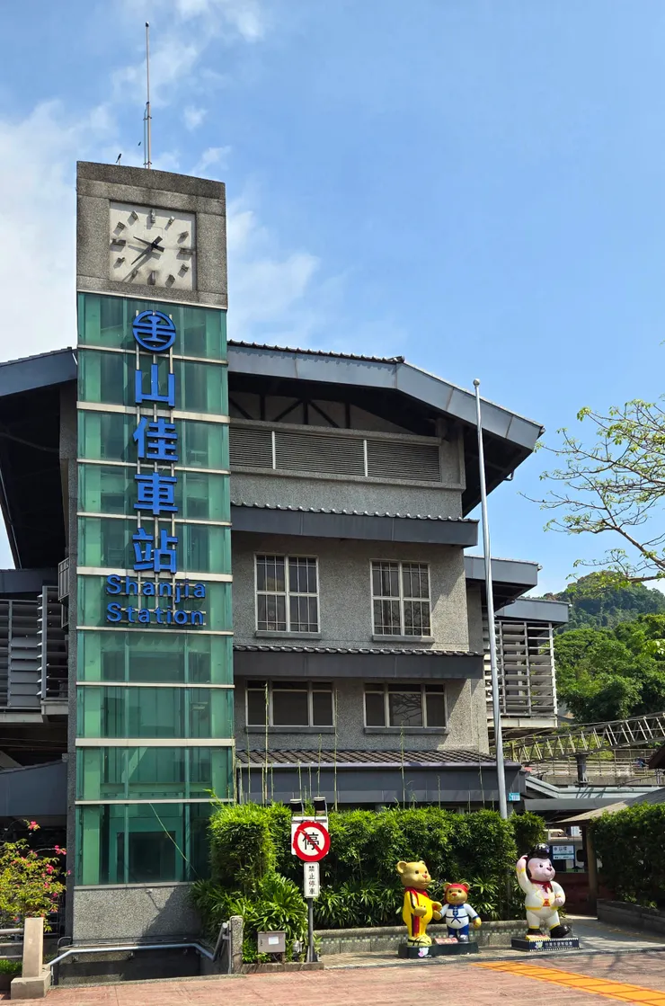 不同於城市灰濛濛的天空,山佳新站大樓頂著湛藍的天空,而時鐘塔指針顯示著已過上班課時段,車站沒有了腳步匆忙的人潮,反而透出慵懶的氣息。三隻泰迪熊公仔在站前看守著站前小廣場,禁止停車標誌豎立牌樓旁。早安,山佳!「這裡,是夢想出發的地方。」