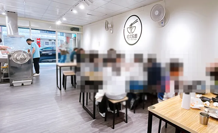 小白拉麵店內環境，純白牆面搭配木質餐桌椅，牆上有初次見面Logo設計，內湖東湖文青風拉麵空間。