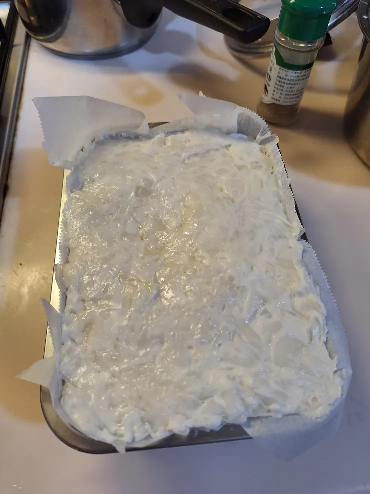 將蘿蔔糕糊倒入鋪好烘焙紙的容器中，用刮刀將表面壓實抹平。